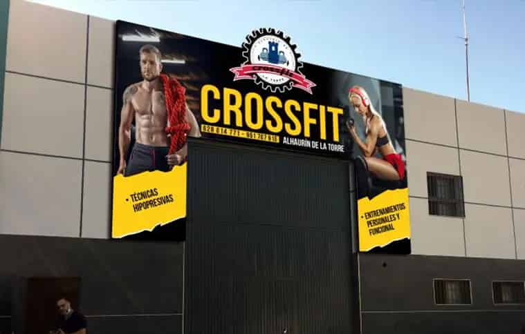 CrossFit gym exterior facade design featuring bold yellow and black branding with fitness model imagery, promotional messaging, and gym logo for Alhaurín de la Torre location.