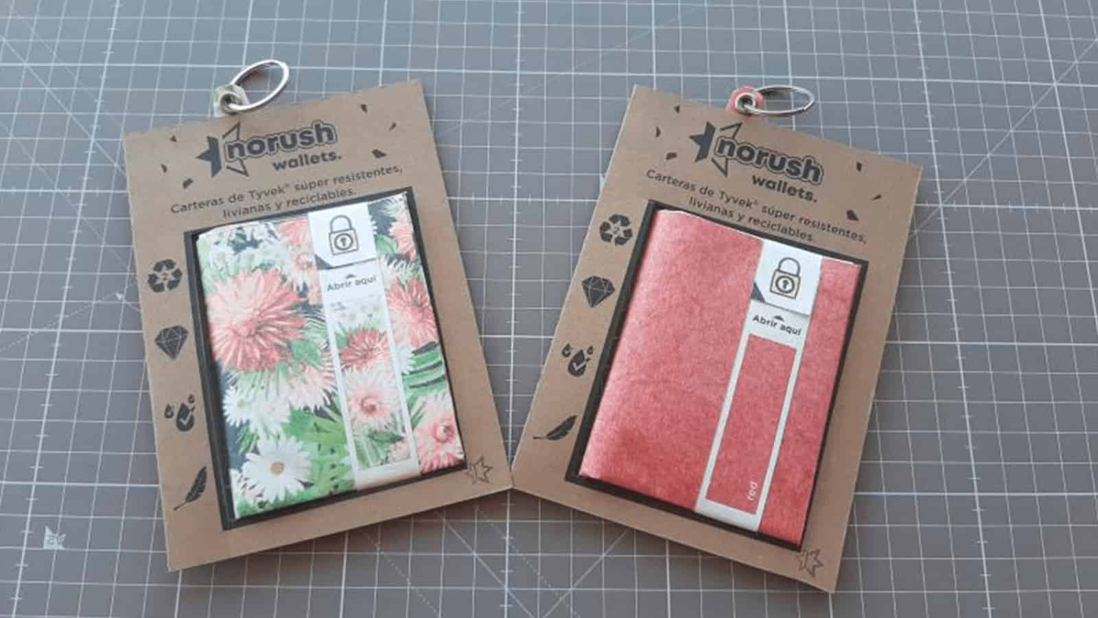 noRush Tyvek® wallets displayed in eco-friendly recycled cardboard packaging with transparent windows showing floral and coral designs.
