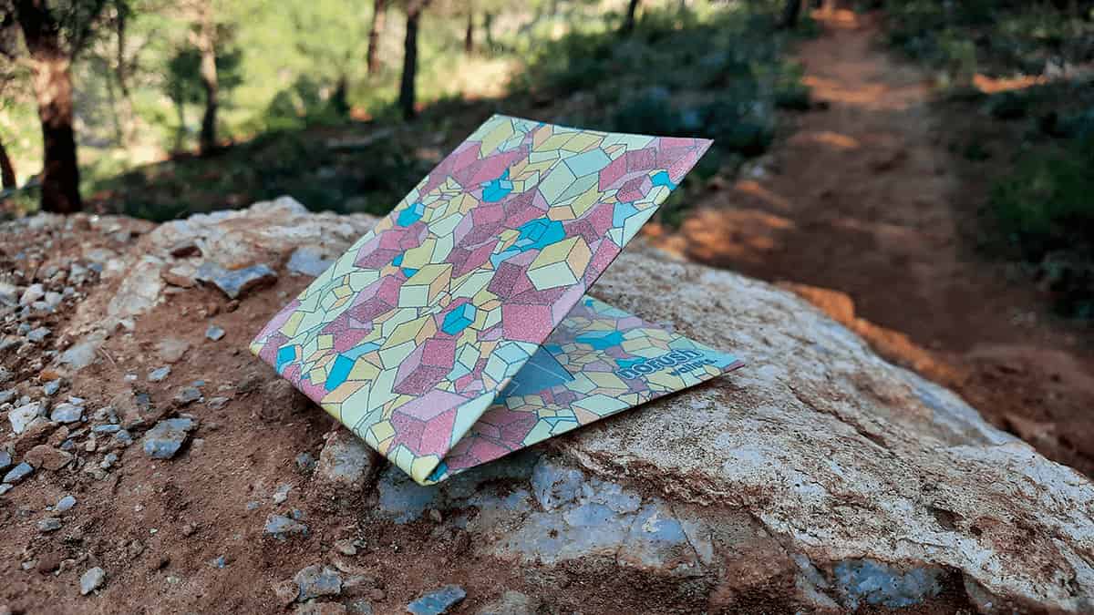 noRush Tyvek® wallet featuring colorful geometric mosaic pattern in pink, blue, and green tones, displayed on natural stone surface.