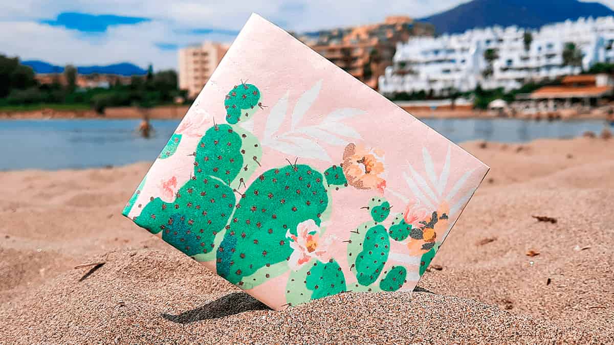 noRush Tyvek® wallet with vibrant green cactus pattern on pink background, photographed on beach sand.